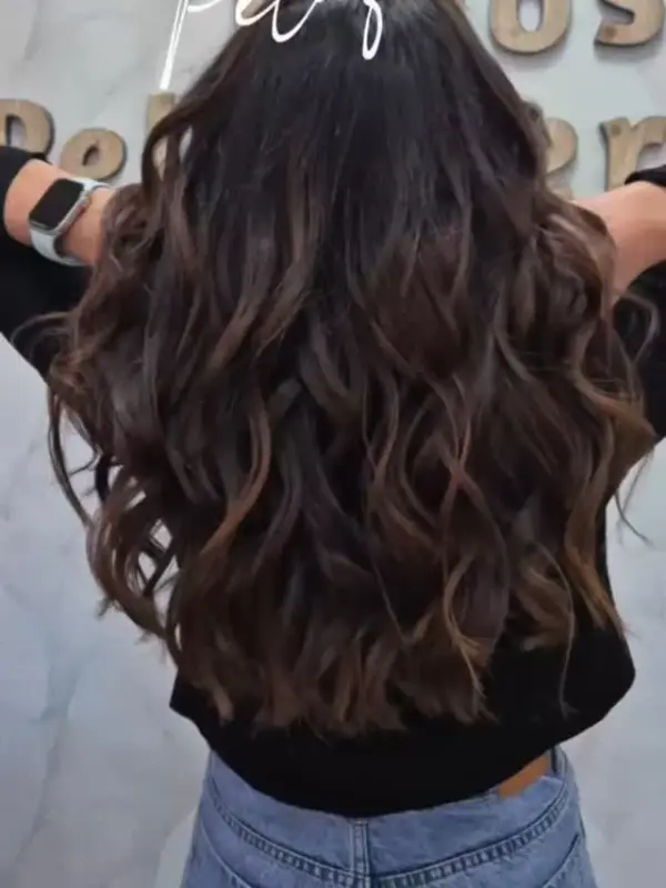 Melena larga morena con ondas, vista de espaldas frente al rótulo de la peluquería